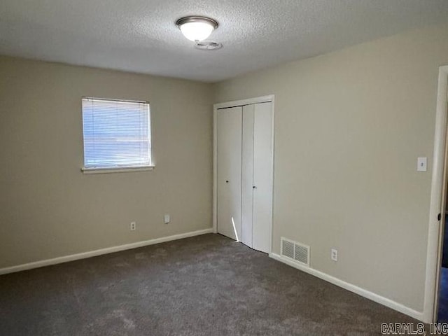unfurnished bedroom with visible vents, baseboards, a closet, dark colored carpet, and a textured ceiling