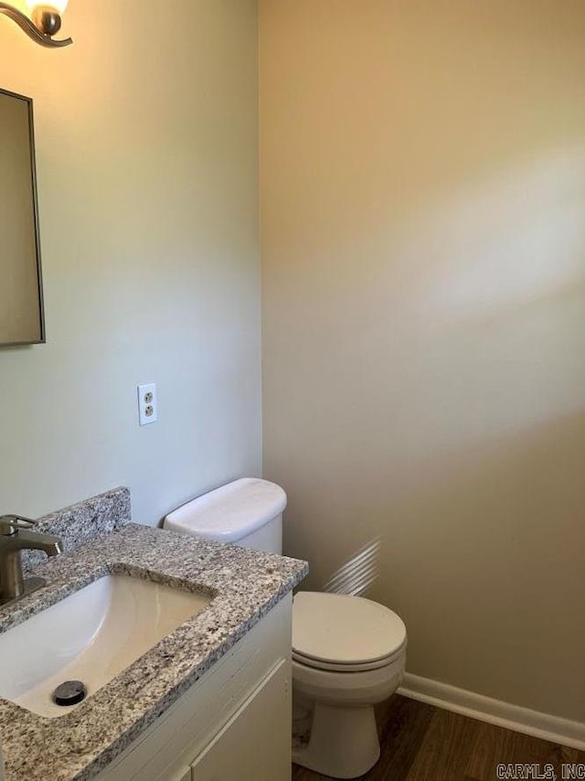bathroom with toilet, wood finished floors, vanity, and baseboards