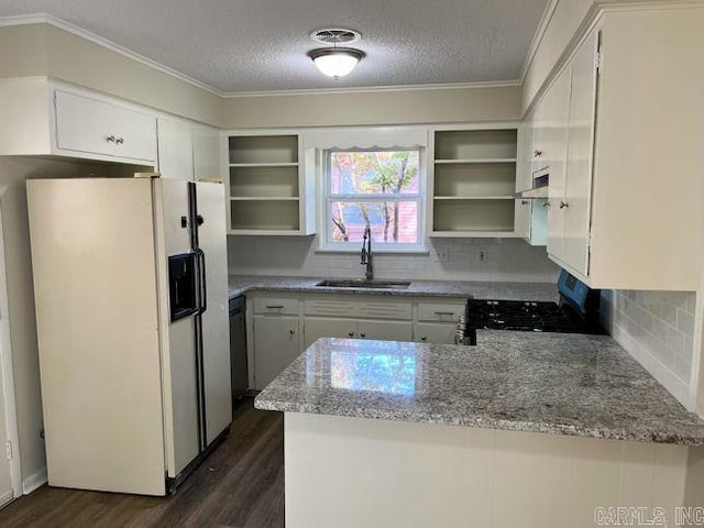 kitchen with gas range oven, white fridge with ice dispenser, a peninsula, open shelves, and a sink