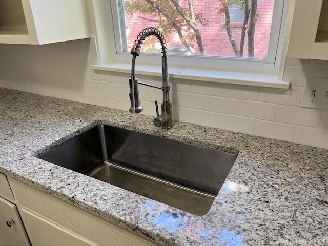 interior details with light stone counters, a sink, backsplash, and white cabinets