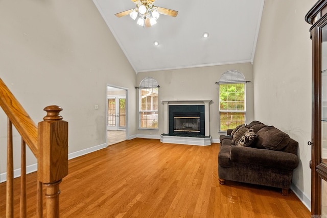 living room with crown molding, a ceiling fan, a tile fireplace, and light wood-style floors