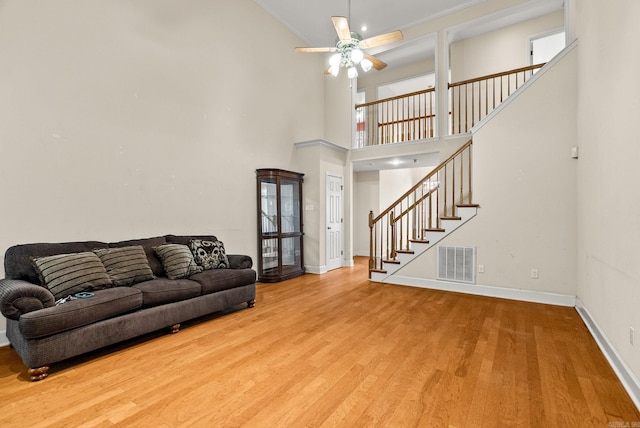living room featuring visible vents, baseboards, a ceiling fan, wood finished floors, and stairs