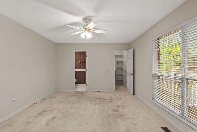unfurnished bedroom featuring ensuite bathroom, light colored carpet, visible vents, a walk in closet, and baseboards
