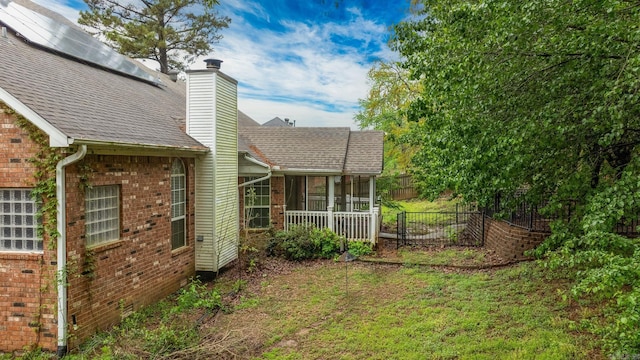 back of house with a shingled roof, a sunroom, a chimney, fence, and brick siding