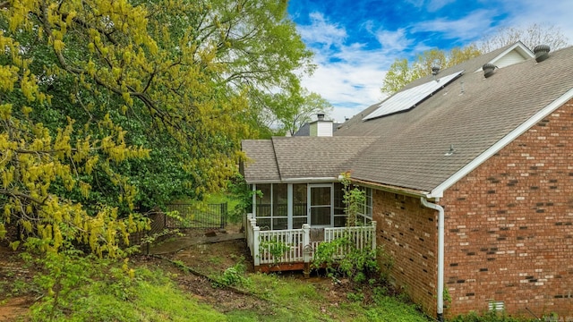 view of property exterior with a sunroom, a chimney, fence, brick siding, and roof with shingles