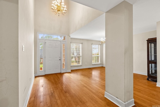 foyer featuring a chandelier, a towering ceiling, light wood-style floors, and baseboards