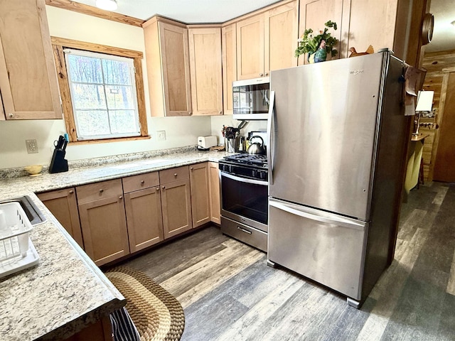 kitchen featuring stainless steel appliances, light stone countertops, light brown cabinets, and wood finished floors