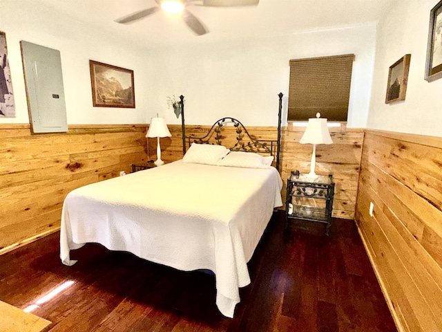 bedroom with wood finished floors, wooden walls, wainscoting, and electric panel