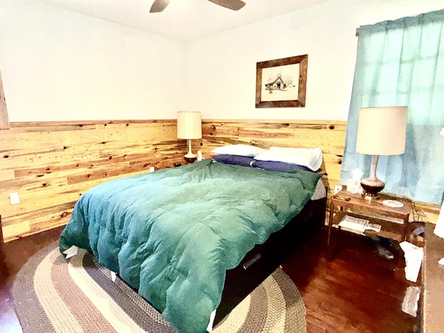 bedroom with wooden walls, ceiling fan, wainscoting, and wood finished floors