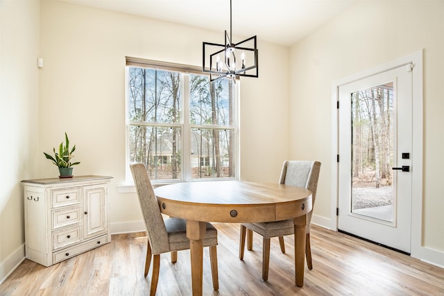 dining area with baseboards, light wood finished floors, an inviting chandelier, and a healthy amount of sunlight