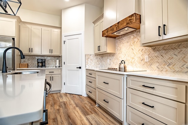 kitchen with a sink, light countertops, premium range hood, and black electric stovetop
