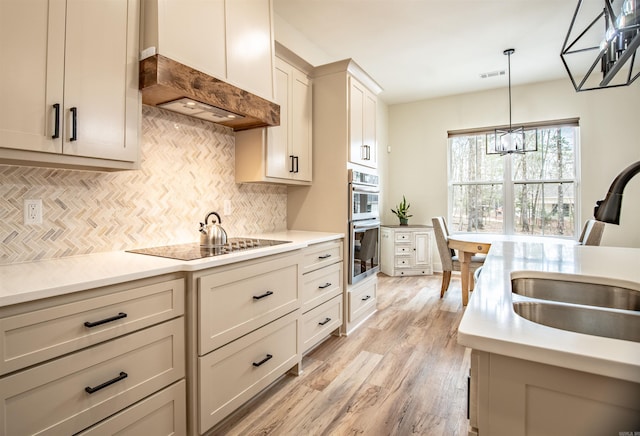 kitchen featuring double oven, visible vents, premium range hood, a notable chandelier, and black electric cooktop