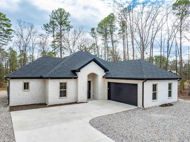 view of front facade with roof with shingles, driveway, a garage, and brick siding