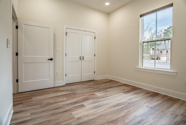 unfurnished bedroom featuring a closet, light wood finished floors, baseboards, and recessed lighting