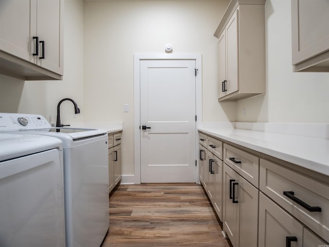 clothes washing area with light wood-style flooring, independent washer and dryer, cabinet space, and a sink