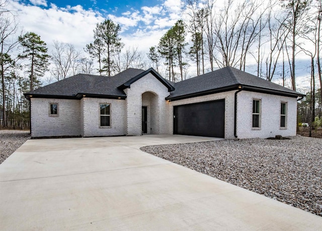view of front of home with a garage, roof with shingles, brick siding, and driveway