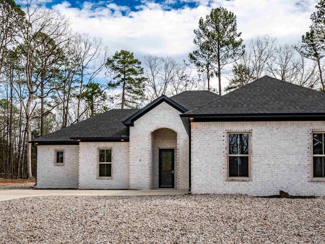 view of front of property featuring brick siding, a patio, and roof with shingles