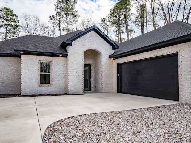 view of front facade with brick siding, a shingled roof, and driveway