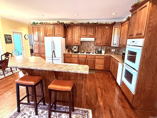 2832 Lacrosse Rd, Melbourne, AR 72556 - kitchen featuring dark wood-style flooring, white appliances, backsplash, under cabinet range hood, and brown cabinetry
