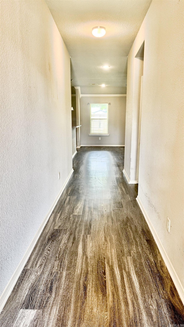 corridor featuring wood finished floors, a textured wall, and baseboards