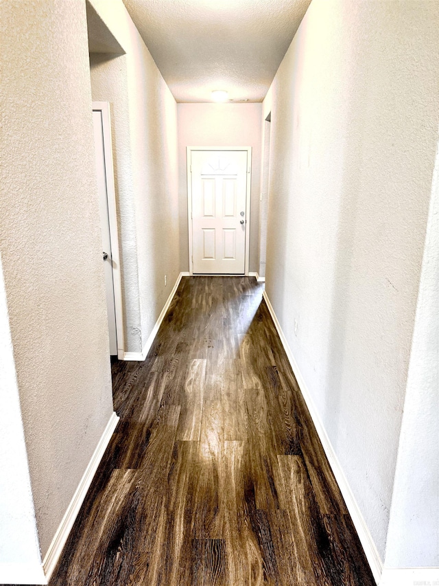 hallway with wood finished floors, a textured wall, and baseboards