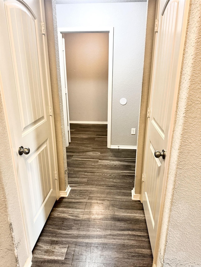hallway with dark wood-style flooring, a textured wall, and baseboards