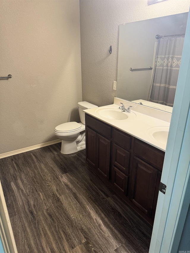 full bathroom with a sink, toilet, double vanity, and wood finished floors