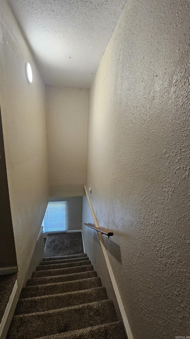 stairway with a textured wall, a textured ceiling, and carpet flooring