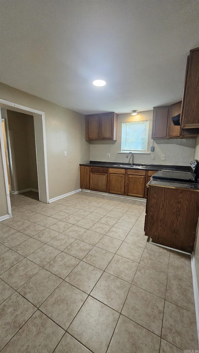 kitchen featuring dark countertops, baseboards, a sink, and light tile patterned floors
