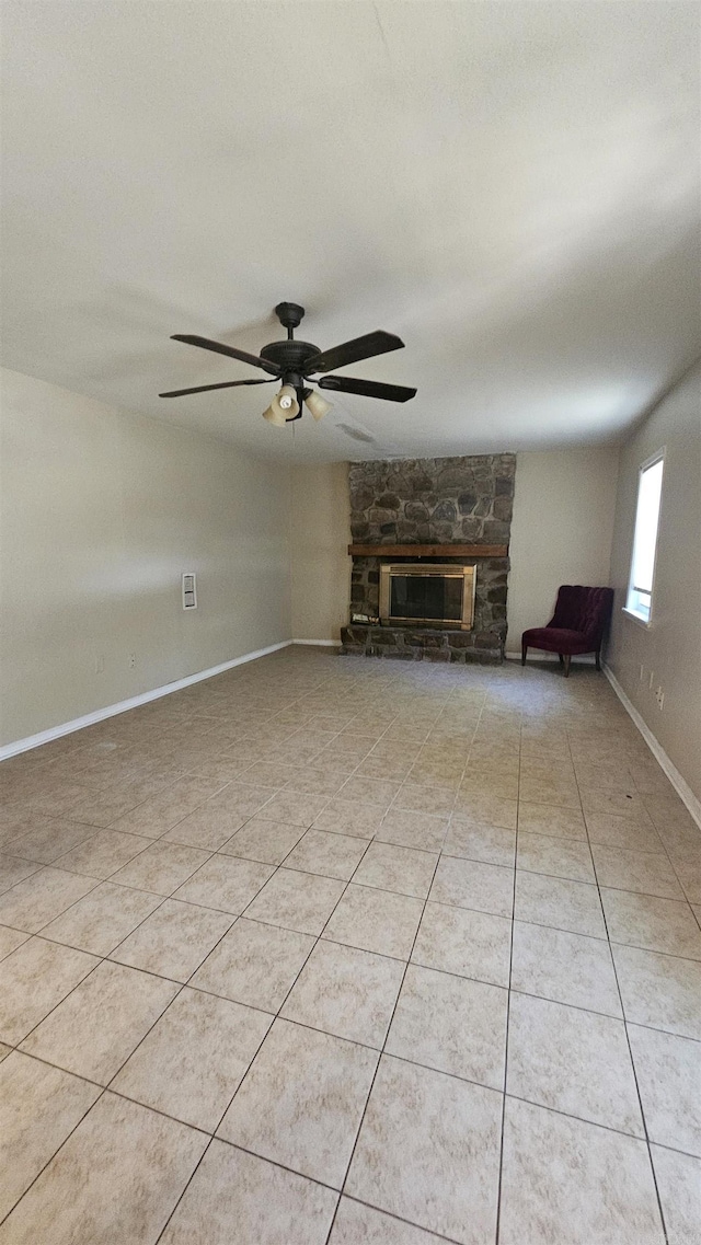 unfurnished living room with ceiling fan, baseboards, light tile patterned flooring, and a stone fireplace