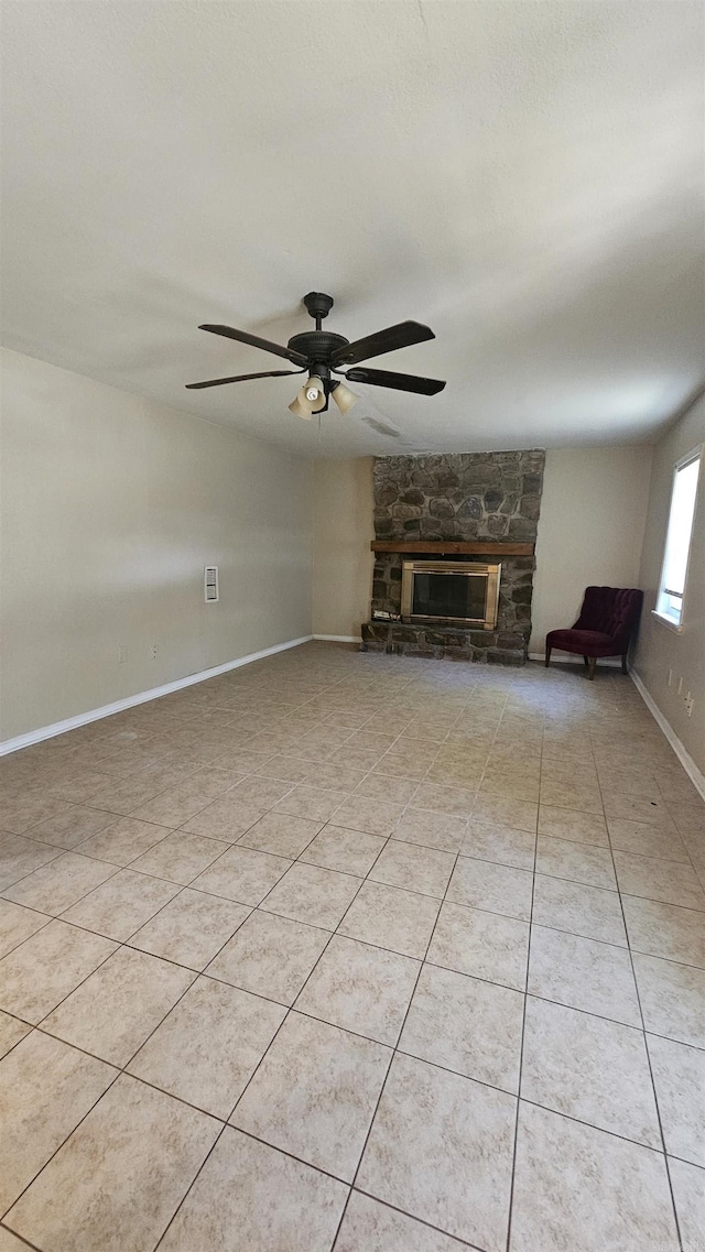 unfurnished living room with light tile patterned floors, baseboards, a stone fireplace, and ceiling fan