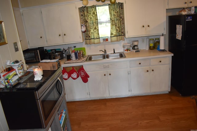 kitchen with freestanding refrigerator, stainless steel microwave, a sink, white cabinetry, and wood finished floors