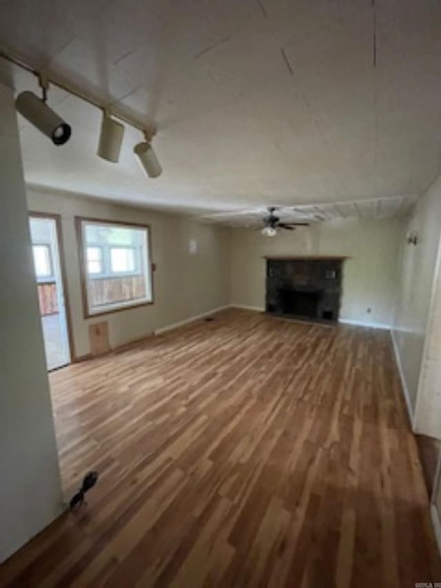 unfurnished living room with baseboards, track lighting, a fireplace, ceiling fan, and wood finished floors