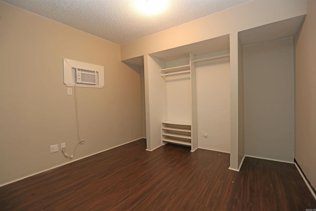 unfurnished bedroom with a textured ceiling, a wall unit AC, a closet, baseboards, and dark wood-style floors