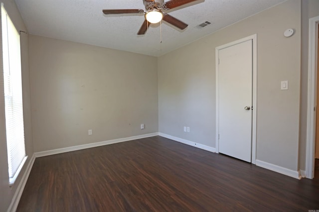 spare room with dark wood-type flooring, a textured ceiling, a ceiling fan, visible vents, and baseboards