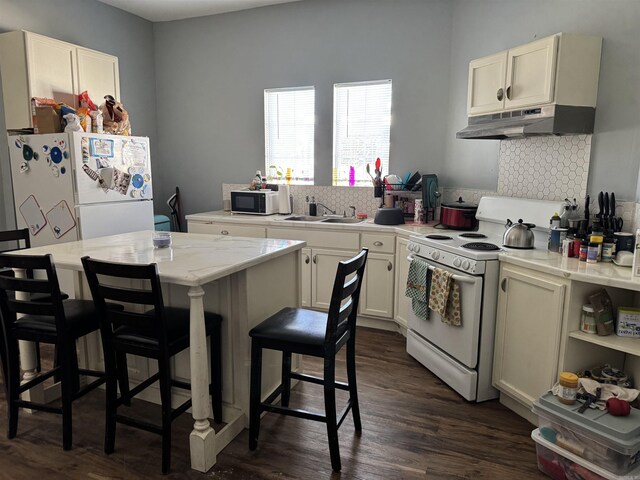 kitchen featuring white appliances, tasteful backsplash, under cabinet range hood, light countertops, and a sink