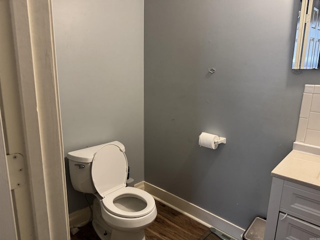 bathroom with toilet, wood finished floors, vanity, and baseboards