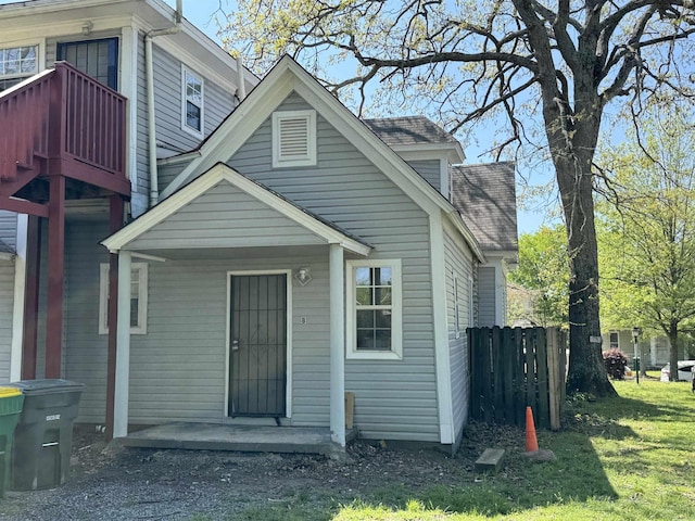 rear view of property with roof with shingles, a balcony, fence, and a lawn