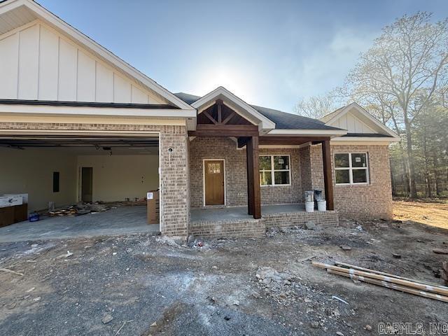 view of front of house with a porch, board and batten siding, a garage, and brick siding
