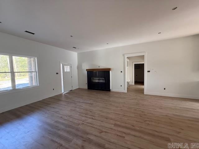 unfurnished living room with a glass covered fireplace, visible vents, baseboards, and wood finished floors