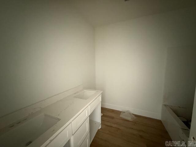 full bath featuring baseboards, double vanity, a bathtub, a sink, and wood finished floors