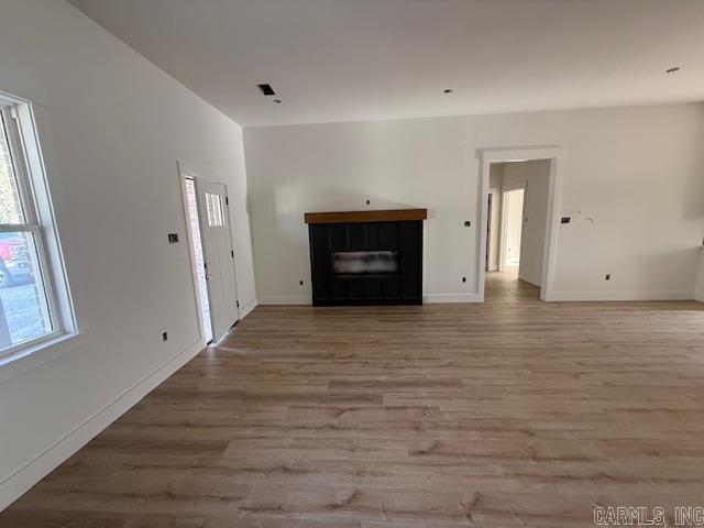 unfurnished living room with light wood-style flooring, a tiled fireplace, and baseboards