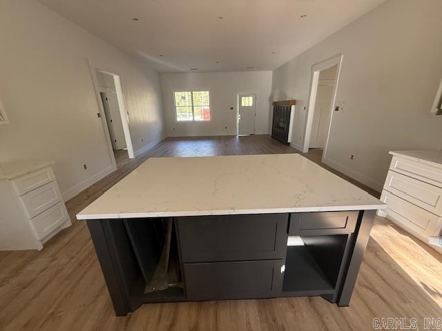 kitchen with dark cabinets, light stone countertops, light wood-type flooring, a kitchen island, and baseboards