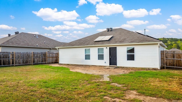 back of property featuring a yard, a fenced backyard, a shingled roof, and solar panels