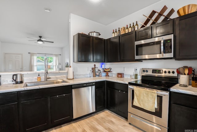 kitchen featuring a sink, light wood-type flooring, a ceiling fan, light stone countertops, and stainless steel appliances