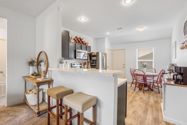 kitchen featuring recessed lighting, a peninsula, light wood-style floors, a breakfast bar area, and stainless steel appliances