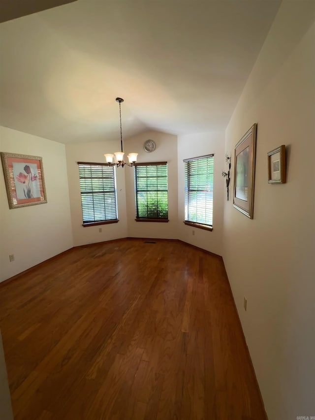 spare room with an inviting chandelier, lofted ceiling, and wood finished floors