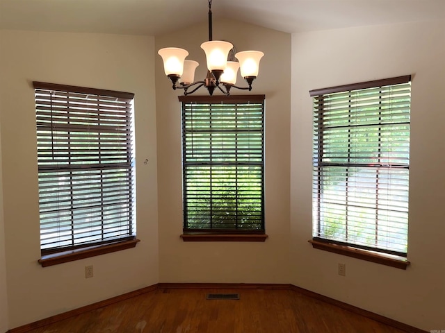 empty room with lofted ceiling, wood finished floors, a wealth of natural light, and a notable chandelier