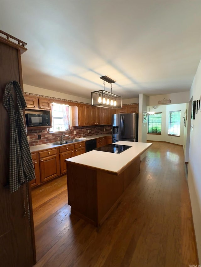 kitchen with a sink, wood-type flooring, a center island, decorative backsplash, and black appliances