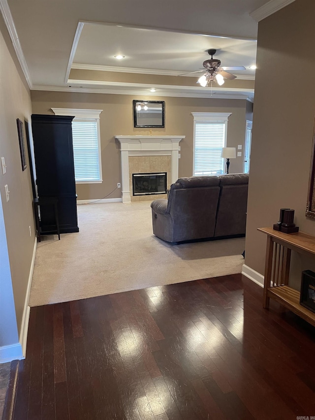living area with baseboards, ornamental molding, a ceiling fan, wood-type flooring, and a tile fireplace
